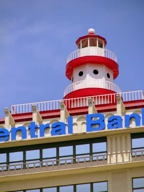 Red and white lighthouse atop a building with "Central Bank" in blue letters against a clear sky.