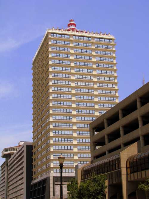 A tall, modern building with a red and white rooftop structure, surrounded by other urban architecture under a clear blue sky.