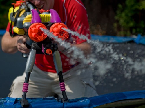 A person in a red shirt sprays water from a colorful toy water blaster on a trampoline.