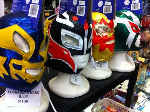 Four colorful luchador masks displayed on white busts, labeled with prices, in a store setting.