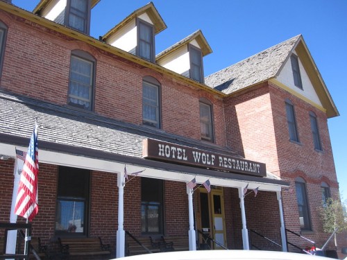 Historic Hotel Wolf Restaurant with brick exterior, yellow trim, and American flags on a clear blue day.