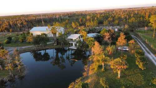 Aerial view of a rural property with a pond, surrounded by trees and a few buildings, during sunset.