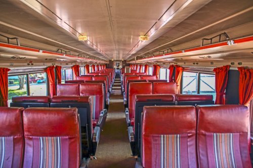 Interior of a bus featuring rows of red and striped seats, with large windows and curtains.