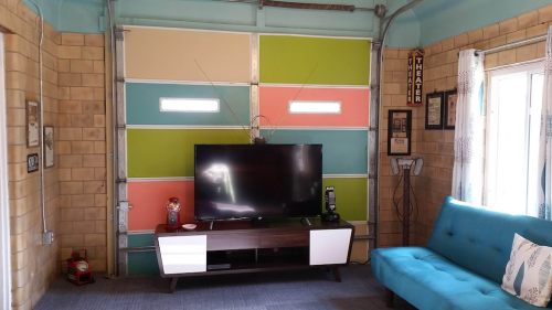 A cozy room with a teal wall, colorful garage door, a TV on a modern stand, and a blue couch.