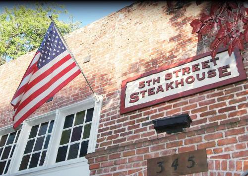 A brick building with a sign reading "5th Street Steakhouse" and an American flag hanging above the entrance.
