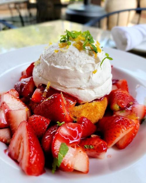 A dessert featuring a cake topped with whipped cream, fresh strawberries, and mint, garnished with orange zest.