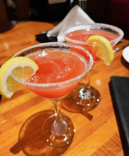 Two cocktails with a sugar rim, garnished with lemon slices, on a wooden table.