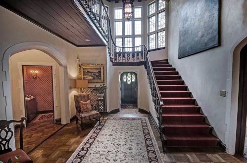 A spacious foyer with a staircase, elegant decor, and large windows, featuring a patterned rug and cozy seating area.