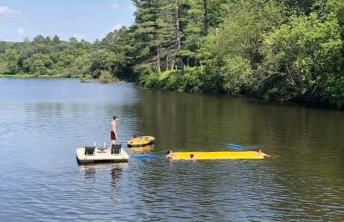 A sunny day at a lake with people swimming and relaxing on a floating platform and inflatable toys.