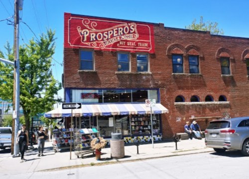 A brick building with a sign reading "Prospero's" features a bookstore and café, with people walking outside.