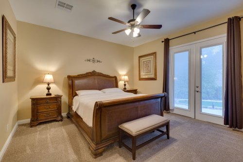 Cozy bedroom with a wooden bed, nightstands, and a bench, featuring warm tones and large windows.