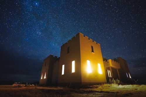 A dimly lit castle-like structure under a starry night sky, with bright windows illuminating the dark surroundings.