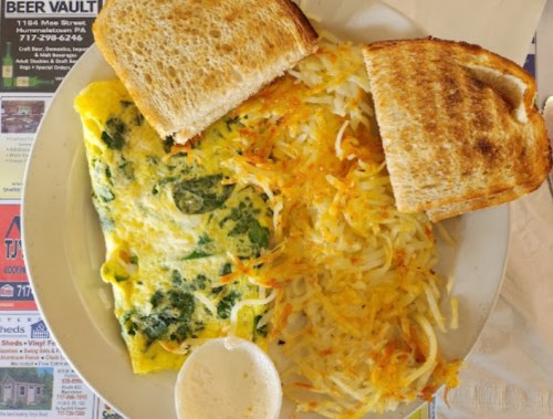 A plate with a spinach omelet, hash browns, and two slices of toasted bread.