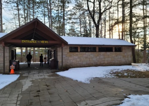 A stone building with a sign reading "Entrance to Views," surrounded by snow and trees, with two people walking nearby.