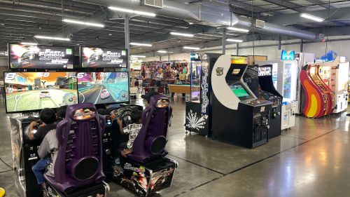 A vibrant arcade with various gaming machines, including racing games and classic arcade cabinets.