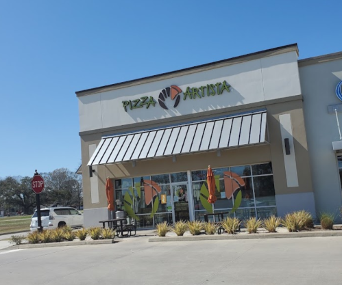 Exterior of Pizza Artista restaurant with colorful signage, outdoor seating, and orange umbrellas on a sunny day.