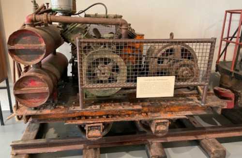 An old, rusty engine displayed on a wooden platform, surrounded by a metal cage for protection.