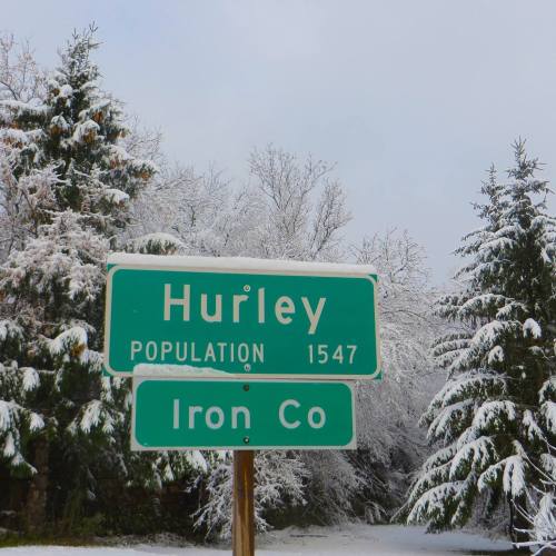Sign for Hurley, Iron County, with a population of 1,547, surrounded by snow-covered trees.