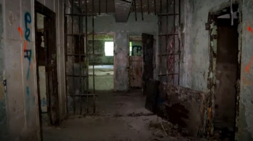 Abandoned interior of a building with peeling walls, graffiti, and barred doorways.