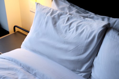 A neatly made bed with white pillows and a soft blanket, illuminated by warm light in the background.
