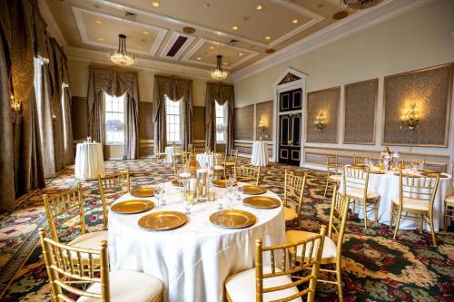 Elegant banquet room with round tables, gold accents, and ornate decor, featuring large windows and a plush carpet.