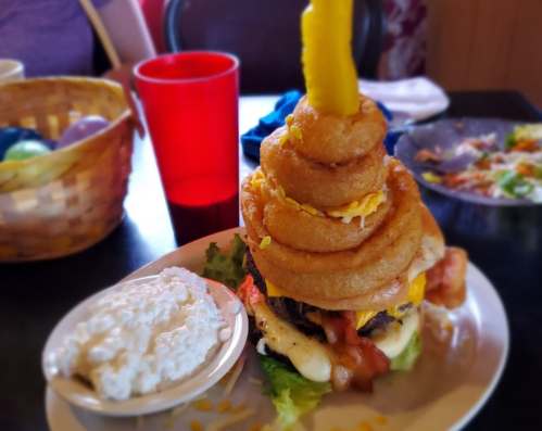 A towering burger topped with onion rings, cheese, and bacon, served with a side of creamy coleslaw.