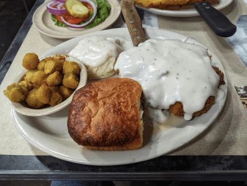 A plate of fried chicken smothered in white gravy, served with biscuits, okra, and a side salad.