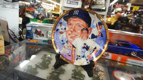 A decorative plate featuring a baseball player in a Yankees uniform, displayed on a stand among collectibles.