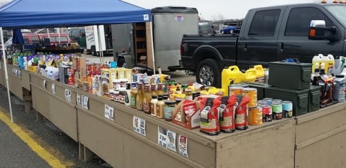 A market stall displaying various food items, condiments, and household products under a blue canopy.