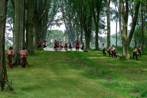 A reenactment scene in a forest, featuring people in historical costumes engaged in a mock battle.