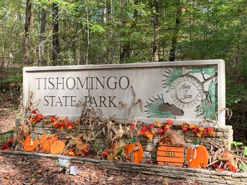 Sign for Tishomingo State Park surrounded by autumn decorations, including pumpkins and colorful leaves.