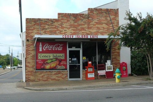 A brick building with a sign for Coney Island Cafe, featuring Coca-Cola branding and a fire hydrant nearby.