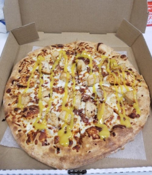 A pizza topped with chicken, cheese, and drizzled with yellow sauce, presented in an open pizza box.