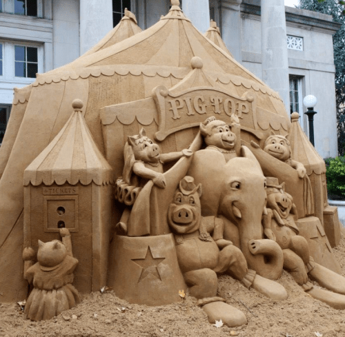 A detailed sand sculpture of a circus tent with animal characters, including pigs and an elephant, in a festive setting.