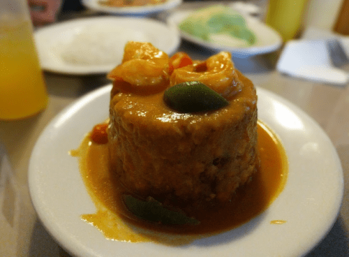 A plate of shrimp served over a mound of rice, topped with a rich, orange sauce and garnished with green peppers.