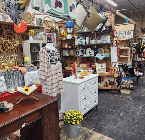 A cozy shop display featuring vintage decor, a mannequin in a dress, and various handmade items on wooden shelves.