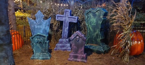 A spooky Halloween scene featuring decorative tombstones, corn stalks, and pumpkins in a dimly lit setting.