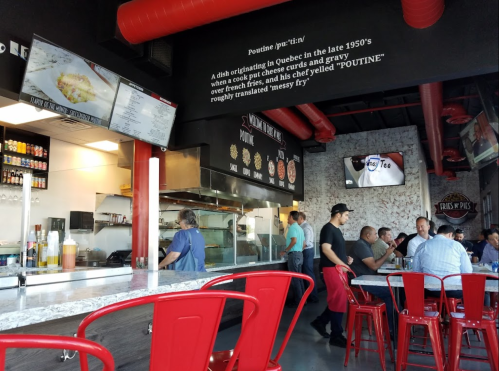 A casual eatery with a modern interior, featuring a counter, menu boards, and patrons enjoying meals at tables.