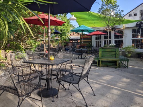 A cozy outdoor seating area with black metal tables and chairs, colorful umbrellas, and lush greenery.