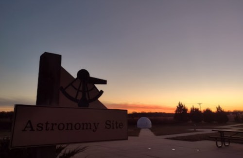 Sign for "Astronomy Site" with a sundial, set against a colorful sunset sky.