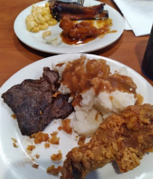 A plate of food featuring fried chicken, mashed potatoes with gravy, beef, and macaroni and cheese.