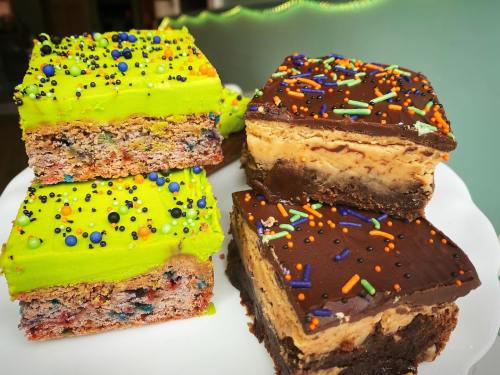 Colorful dessert squares with vibrant green frosting and chocolate layers, topped with sprinkles on a white plate.