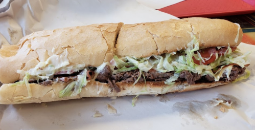 A large sandwich filled with sliced beef, lettuce, tomatoes, and mayonnaise, served in a toasted hoagie roll.
