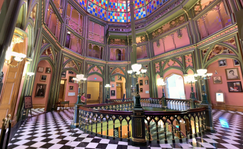 Colorful interior of a historic building featuring ornate arches, stained glass, and a checkered floor.