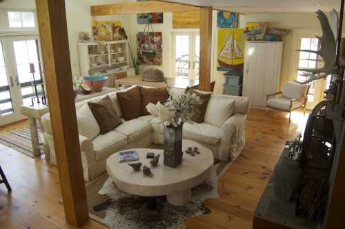 A cozy living room with a white sofa, wooden accents, and colorful artwork on the walls, featuring a round coffee table.