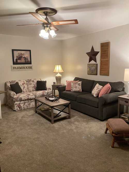 Cozy living room with floral and gray sofas, a wooden coffee table, lamps, and farmhouse decor on the walls.