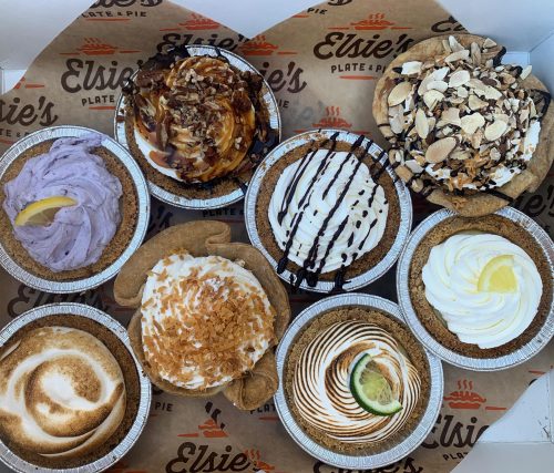 A variety of delicious pies in individual tins, featuring different toppings and flavors, arranged in a box.