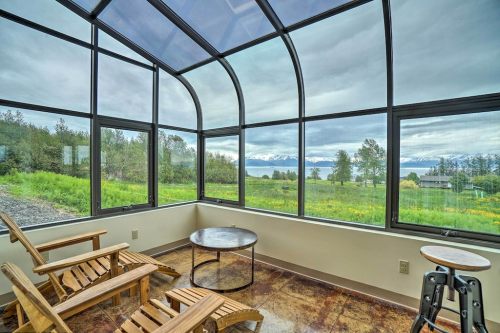 A cozy sunroom with wooden chairs and a table, offering a view of mountains and greenery through large windows.