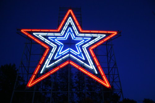 A large illuminated star sign in red, white, and blue against a dark blue sky.