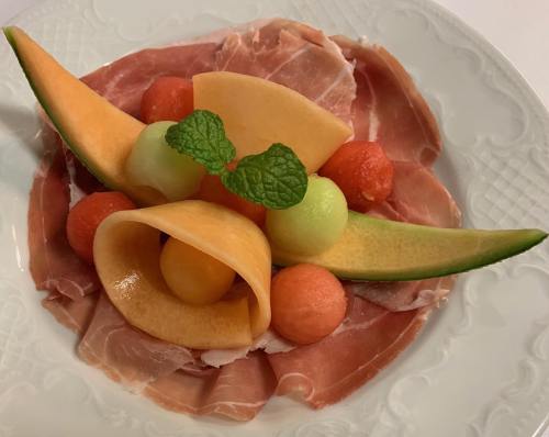 A plate of prosciutto topped with melon slices and balls of cantaloupe and honeydew, garnished with mint leaves.